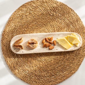 Könnte beinhalten: Ein rechteckiges, cremefarbenes Serviertablett mit Feigen, Mandeln und Käse. Das Tablett steht auf einem runden, gewebten, naturfarbenen Platzset. Das Essen ist in separaten Abschnitten auf dem Tablett angeordnet.