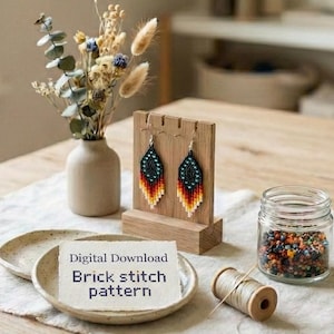 Könnte beinhalten: Ein Holztisch zeigt Perlenohrringe auf einem Holzständer, eine kleine Vase mit Trockenblumen, einen kleinen Teller mit einer Karte mit der Aufschrift "Digital Download Brick stitch pattern", ein Glas mit Perlen und eine Garnrolle. Die Ohrringe sind schwarz, orange und gelb.