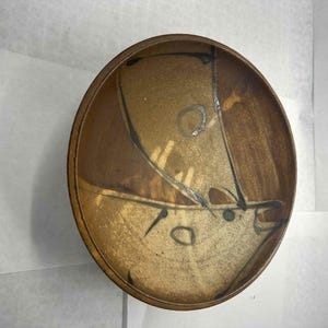 Könnte beinhalten: Eine handgefertigte Keramikschale mit einem einzigartigen abstrakten Design. Die Schale hat eine Mischung aus Braun- und Beigetönen mit schwarzen und silbernen Akzenten. Das Innere hat ein helleres, gesprenkeltes Aussehen, während der Rand dunkelbraun ist. Diese dekorative Schale eignet sich zum Servieren oder Ausstellen.