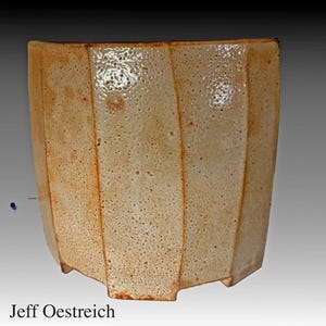 May include: A handcrafted, beige ceramic planter with a geometric, faceted design. The planter has a square base and a slightly flared top. The surface has a speckled texture and a glossy finish. The artist's name, "Jeff Oestreich", is at the bottom.