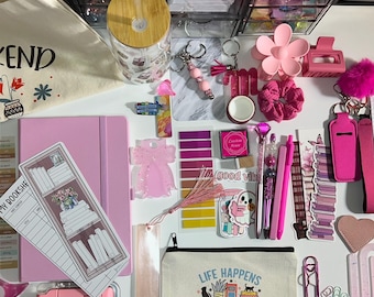 May include: A collection of pink and white stationery and accessories, including a tote bag with text, a pink notebook, pens, stickers, a pouch with text, and a glass with a wooden lid. The items are arranged on a white surface.