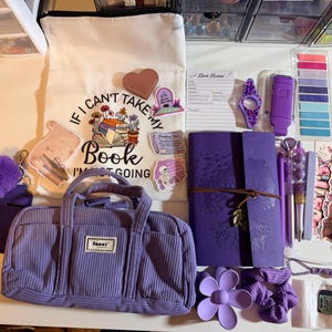 Op de afbeelding: Een assortiment paarse briefpapier en accessoires, waaronder een corduroy tas, een draagtas met de tekst "If I can't take my book I'm not going", een notitieboek, pennen, stickers en een horloge. De items zijn gerangschikt op een wit oppervlak.