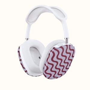 May include: White over-ear headphones with a padded headband and earcups. The earcups feature a wavy, maroon pattern on a light purple background. The headphones have a modern design and are set against a plain background.