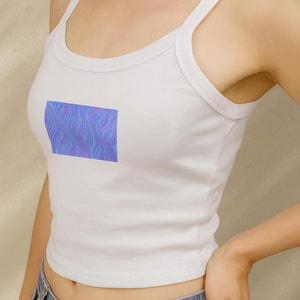 Könnte beinhalten: Weißes Tanktop mit einem rechteckigen Design auf der Vorderseite. Das Design zeigt ein wellenförmiges Muster in Blau-, Lila- und Rosatönen. Das Top hat einen Rundhalsausschnitt und Spaghettiträger.