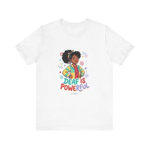 Puede incluir: Camiseta blanca con una colorida ilustración de una niña y el texto "DEAF IS POWERFUL". La niña lleva una chaqueta amarilla, una camisa roja y una diadema estampada. El diseño incluye estrellas y espirales.