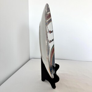 Puede incluir: Un plato de cer&aacute;mica blanco con un borde decorativo que presenta un dise&ntilde;o colorido de patrones rojos, azules y dorados. El plato se exhibe sobre un soporte negro, mostrando su perfil lateral sobre un fondo blanco.