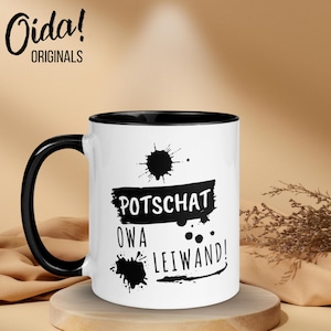 May include: White ceramic mug with a black handle and rim. The mug features the text "Potschat Owa Leiwand!" in black, along with black splatter designs. The mug is branded with the "Oida! ORIGINALS" logo.