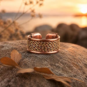 May include: A copper ring featuring an open-ended design with a central band of braided wire. The ring has smooth, solid copper edges at the top and bottom, contrasting with the intricate, textured metallic weave of the middle section.