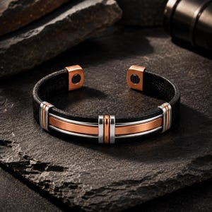 Puede incluir: Una pulsera tipo brazalete con una banda negra texturizada acentuada por tiras metálicas centrales en tonos cobre y plata. El diseño abierto incluye tapas de extremo en tono cobre con inserciones magnéticas circulares oscuras en el interior.