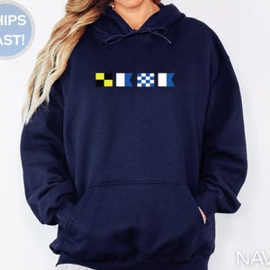 May include: Navy blue hoodie with a front pocket and a drawstring hood. The hoodie features a design of colorful flags across the chest. The words "SHIPS FAST!" are in a blue circle in the upper left corner. The word "NAVY" is in the lower right corner.