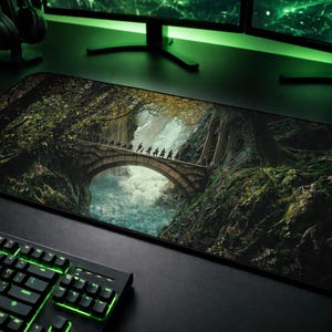 以下が含まれることがあります： ファンタジーの風景が描かれた長方形のマウスパッド。川にかかる石橋があり、その上を人物が歩いている。マウスパッドは黒いキーボードとコンピューターモニターに囲まれている。