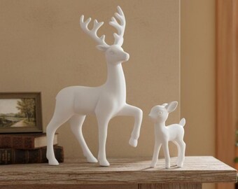 May include: Two white ceramic deer figurines. One is a large adult deer with raised front leg and large antlers. The other is a smaller fawn. Both are on a wooden surface.