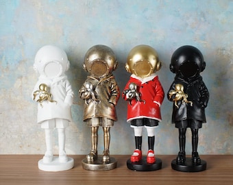 May include: Four decorative figurines of children in diving suits, each holding a golden octopus. The figurines are in white, gold, red, and black. The diving helmets have open faceplates. The figurines are standing on a wooden surface.