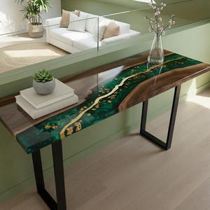 Puede incluir: Una consola moderna con una tapa de madera oscura y un vibrante diseño de río de resina epoxi verde y dorado. La mesa tiene patas de metal negro y está colocada en una habitación bien iluminada. La mesa mide 152 cm de largo.