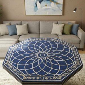 May include: An octagonal coffee table with a blue surface and a white geometric floral design. The table is in front of a grey sectional sofa with decorative cushions. The room has a neutral colour palette.