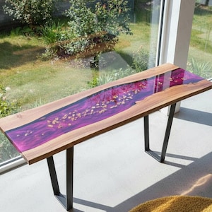 Op de afbeelding: Een rechthoekige houten console met een levendig paars harsmiddelpunt en goudbladaccenten. De tafel heeft een natuurlijke houtnerfrand en zwarte metalen poten. De tafel is ongeveer 152 cm lang.