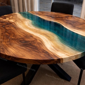 May include: A round wooden table with a unique design. The table features a river of blue and tan resin flowing through the center of the wood. The table is supported by a black metal base and is surrounded by black chairs.