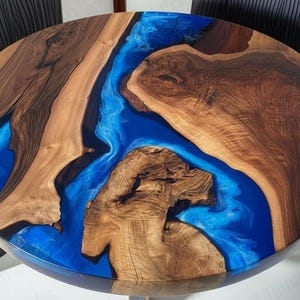 Puede incluir: Mesa redonda de madera con un diseño de río de resina epoxi azul. La mesa presenta un patrón de vetas de madera natural con un acabado brillante. La mesa tiene aproximadamente 122 cm de diámetro.