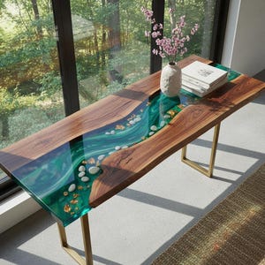 Puede incluir: Mesa de madera artesanal con diseño de río. El centro es de resina epoxi transparente de color turquesa con piedras y escamas doradas. La mesa se apoya en patas de metal color dorado.