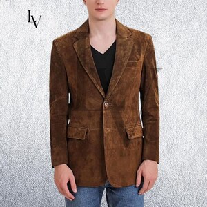 May include: A brown suede blazer with a notched lapel, two front pockets, and a single-button closure. The jacket is worn over a black V-neck shirt. The blazer is a classic style.