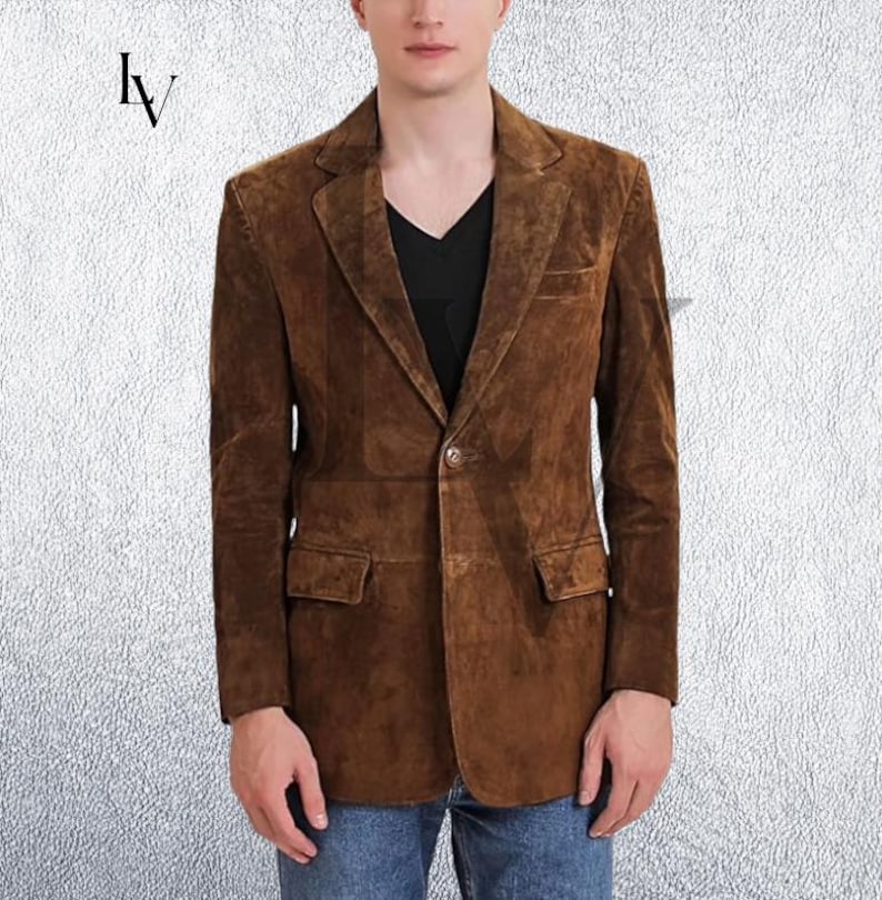 May include: A brown suede blazer with a notched lapel, two front pockets, and a single-button closure. The jacket is worn over a black V-neck shirt. The blazer is a classic style.