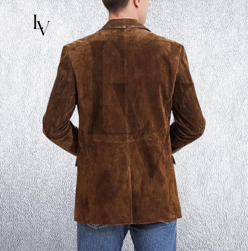 May include: A brown suede blazer with a classic two-button closure. The jacket features a notched lapel and two front pockets. The back view shows the tailored fit and the soft texture of the suede. The blazer is worn with blue jeans.