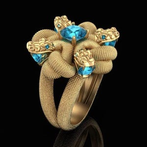 May include: A gold ring with a design of intertwined snakes. Each snake head has a blue gemstone eye, and a larger blue gemstone is set in the centre. The ring is set against a black background.