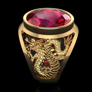 Puede incluir: Un anillo dorado con una gran piedra preciosa roja de forma ovalada. El anillo presenta un diseño detallado de dragón dorado en los laterales. El anillo está sobre un fondo negro, resaltando los intrincados detalles de la joya.
