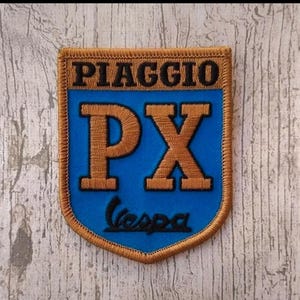 Può includere: Toppa ricamata con il logo Piaggio Vespa. La toppa ha uno sfondo blu con le lettere "PX" dorate e il testo "Vespa" in nero. Il bordo e la parola "PIAGGIO" sono dorati.