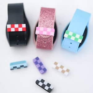 May include: Three smart watch bands in black, pink glitter, and light blue, each with a checkered accent in red and white, pink and white, and green and white. Additional checkered accents in blue, purple, and tan are also present.
