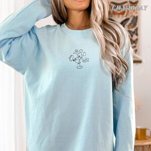 Op de afbeelding: Een lichtblauwe sweatshirt met een zwarte lijntekening van een stripfiguur. Het woord "Oh" staat boven het figuur. De longsleeve is gemaakt van een zacht materiaal.