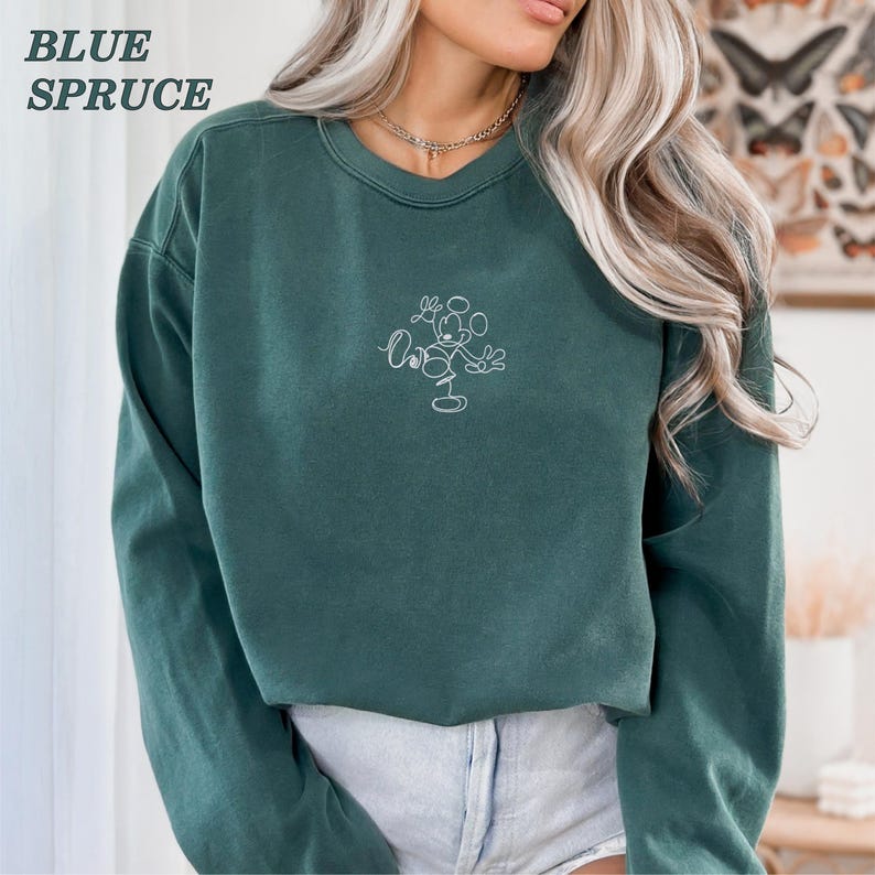 Op de afbeelding: Blauwspar sweatshirt met een witte omtrek van Mickey Mouse. De sweatshirt heeft een ronde hals en lange mouwen. De woorden "BLUE SPRUCE" staan in de linkerbovenhoek gedrukt.