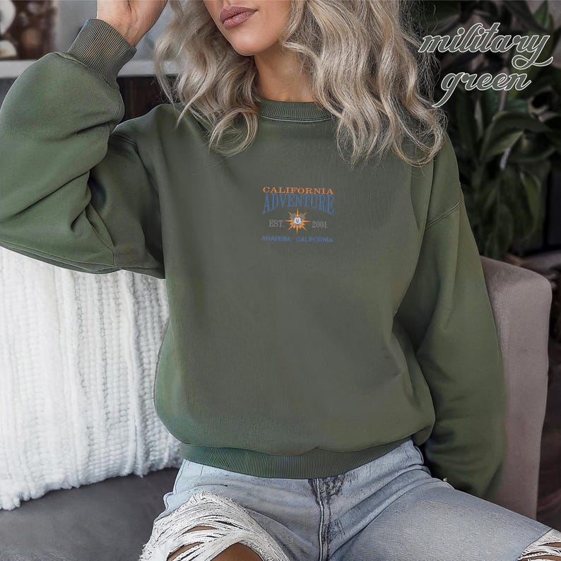 Pu&ograve; includere: Felpa verde militare con la scritta "CALIFORNIA ADVENTURE" e una grafica a forma di sole. La felpa ha un girocollo e maniche lunghe. Il testo "EST. 2001" e "ANAHEIM, CALIFORNIA" sono stampati anche sul davanti.