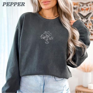 Op de afbeelding: Een antracietgrijs sweatshirt met een wit geborduurd Mickey Mouse-ontwerp. Het woord "PEPPER" staat linksboven gedrukt. De sweatshirt heeft lange mouwen en een ronde hals.