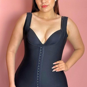 Könnte beinhalten: Schwarze Ganzkörper-Shapewear mit tiefem V-Ausschnitt und Haken-Ösen-Verschluss vorne. Das Kleidungsstück hat breite Träger und reicht bis zur Mitte der Oberschenkel mit Spitzenbesatz. Es ist für eine glatte, konturierte Silhouette konzipiert.