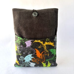 May include: A rectangular pouch featuring a dark brown corduroy upper section with a single centered button closure. The lower section is made of a dark fabric printed with a repeating pattern of colorful dragons in shades of green, orange, yellow, and light blue.