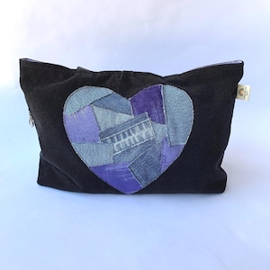 May include: Black corduroy zippered pouch with a patchwork heart design in shades of blue and purple. The heart is made from denim fabric. The pouch has a small tag attached to the side.