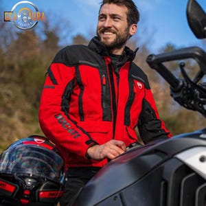 Puede incluir: Chaqueta de moto roja y negra con la palabra "DUCATI" impresa en la manga. La chaqueta tiene múltiples bolsillos y un cuello alto. Se ve un casco de moto negro con detalles rojos.