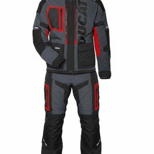 Pode incluir: Conjunto de jaqueta e calças de moto cinza e preto com detalhes em vermelho. A jaqueta apresenta a palavra "DUCATI" em letras cinzas grandes. O conjunto inclui vários bolsos e uma gola alta.