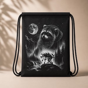 May include: A black drawstring backpack featuring a white graphic print of a large raccoon face above a smaller raccoon walking on a rock near a forest, a waterfall, and a full moon in a starry night sky. The bag has black cord shoulder straps.