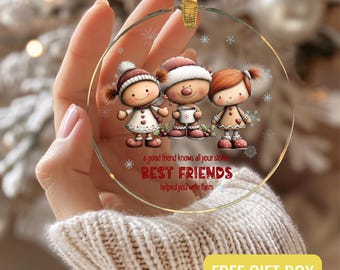 Puede incluir: Un adorno navideño de cristal transparente con una cinta dorada. El adorno presenta tres figuras de dibujos animados con ropa de invierno, con el texto "BEST FRIENDS" y una cita. También hay diseños de copos de nieve.