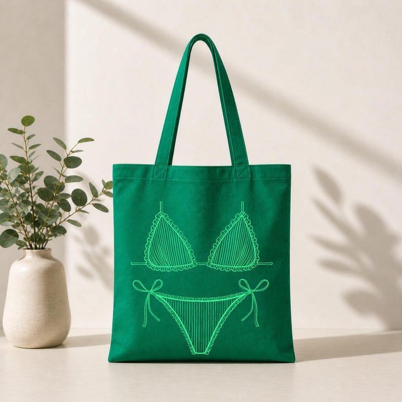 May include: A green tote bag featuring a neon green outline of a bikini. The bikini top has a scalloped edge and the bottoms have tie details. The bag has two green handles and is made of a sturdy fabric, perfect for carrying beach essentials.