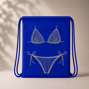 May include: A royal blue drawstring bag featuring a gold-colored line drawing of a bikini. The bikini top and bottom are detailed with vertical stripes and scalloped edges. The bag has blue drawstrings.