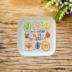 Könnte beinhalten: Eine weiße Keramik-Tasse mit schwarzem Henkel und dem Text "But First, Coffee" in schwarzer, handschriftlicher Schrift. Die Tasse steht auf einer weißen Oberfläche.