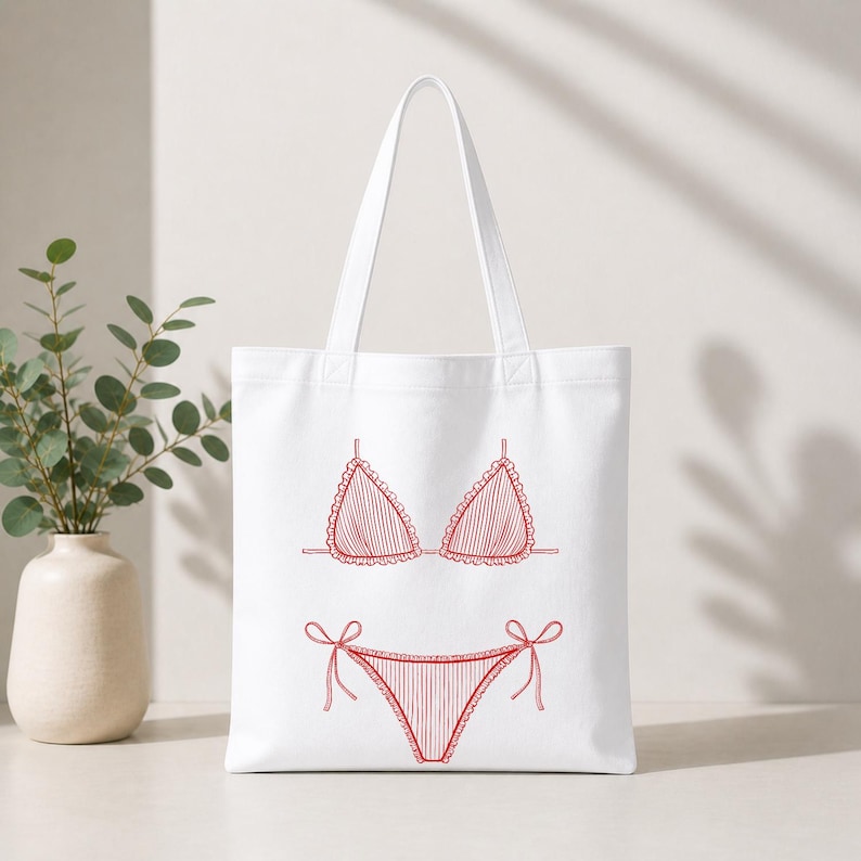 May include: White tote bag featuring a red line drawing of a bikini. The bikini top has a triangle shape with ruffled edges, and the bottom has tie sides. The bag has a simple design, perfect for carrying beach essentials.