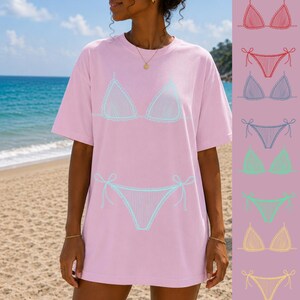 May include: A light pink t-shirt featuring a light blue bikini design. The bikini design includes a triangle top and a bottom with tie details. The image also shows a variety of bikini colors, including red, purple, green, and yellow.