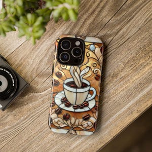 May include: A phone case with a coffee cup design and coffee beans. The case has a stained glass style with brown, beige, and white colours. The phone case is on a wooden surface.