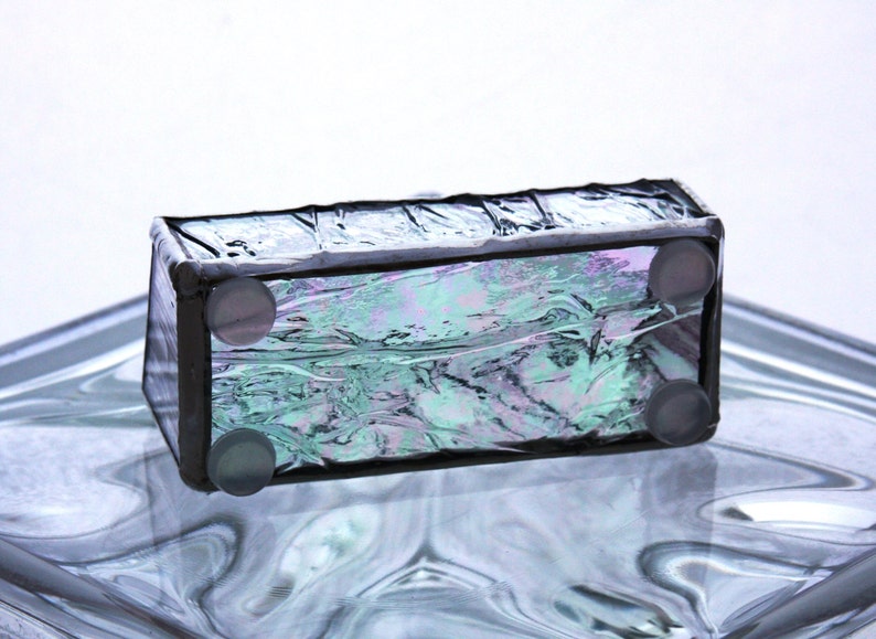 Peut inclure: Une petite bo&icirc;te rectangulaire en verre avec un cadre noir et un verre iridescent bleu, vert et violet. La bo&icirc;te a quatre pieds en caoutchouc sur le fond.