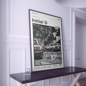 Può includere: Un poster incorniciato di Initial D con un'illustrazione in bianco e nero in stile manga di due auto da corsa. Il poster include il testo "Initial D" e l'anno "1995". Il poster è esposto su un tavolo scuro.