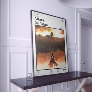 Op de afbeelding: Een ingelijste poster met de titel "Attack On Titan" in zwarte letters. De afbeelding toont een silhouet tegen een vurige, oranje en bruine achtergrond. Het jaar "2009" is zichtbaar in de rechterbenedenhoek.